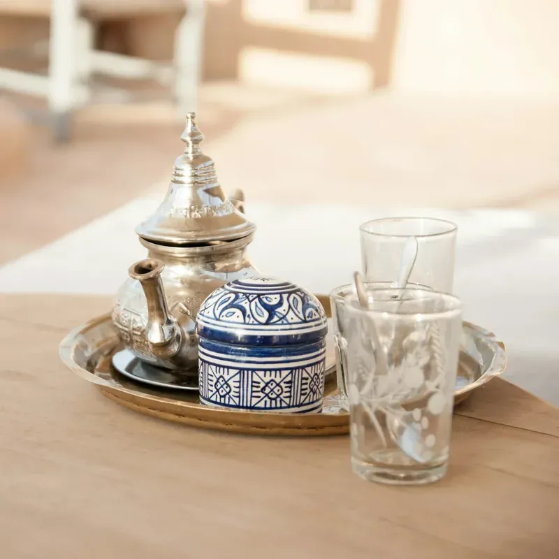 Théière marocaine argentée, sucrier en céramique bleue et blanche et verres à thé sur un plateau