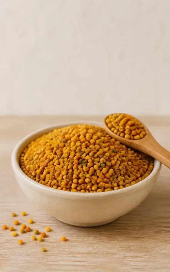 Bol en céramique rempli de pelotes de pollen jaune orangé, avec une cuillère en bois, sur une table en bois clair