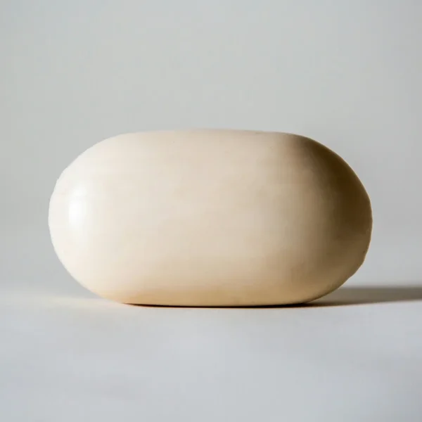 Pain de savon blanc ivoire aux bords arrondis, sur fond gris clair