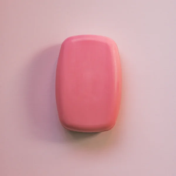 Pain de savon rose aux bords arrondis, sur fond rose clair