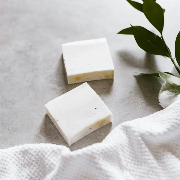 Deux pains de savon blancs à côté d’une serviette éponge et d’un rameau de feuillage
