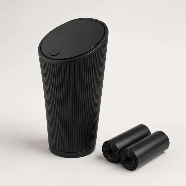 Poubelle de voiture en plastique noir mat strié, évasée vers le haut, couvercle ovale en biais avec bouton-poussoir, à côté de deux rouleaux de sacs noirs