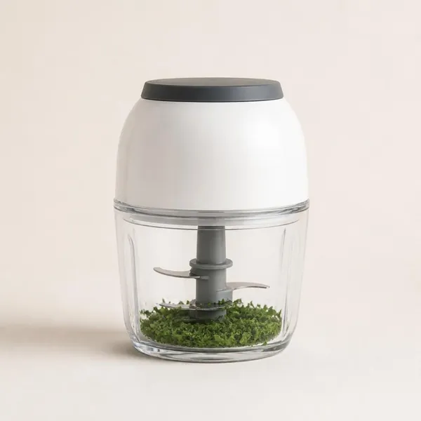 Mini-hachoir électrique au bloc moteur blanc arrondi sur un bol transparent avec du persil haché